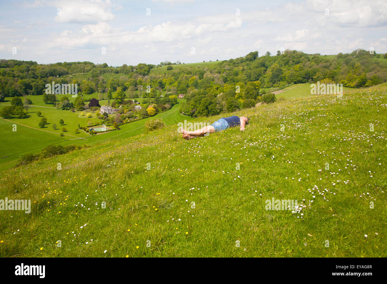Woman lying on chalk grassland looking into deep green valley containing Rainscombe House, Oare Hill, Wiltshire, England, UK Stock Photo