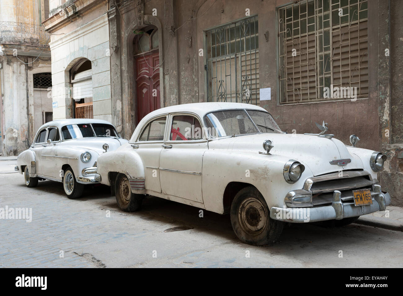 HAVANA, CUBA - JUNE, 2011: Pair of classic American cars in matching white stand parked on a typically quiet street in Centro. Stock Photo