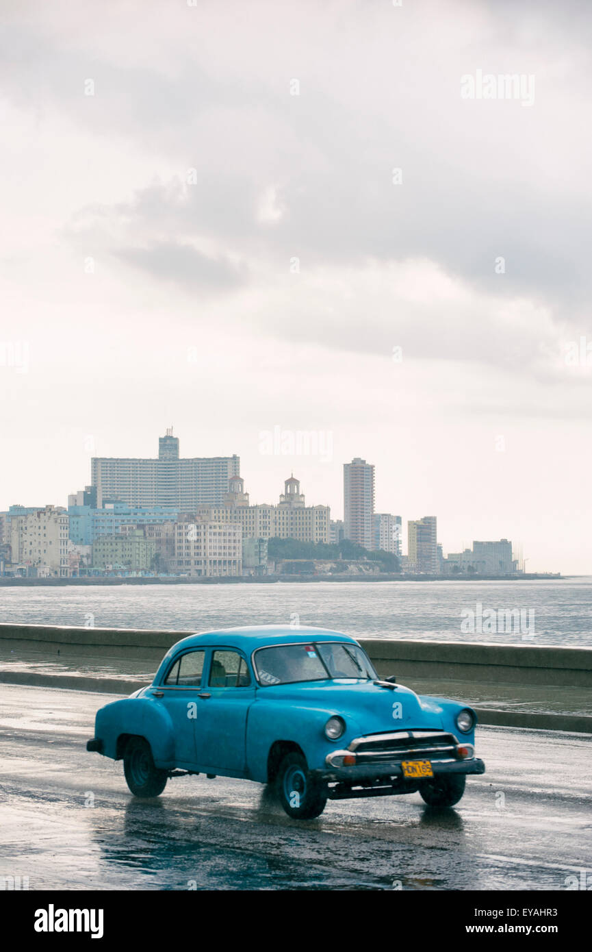 HAVANA, CUBA - JUNE 13, 2011: Classic old fashioned 50s car passes in front of the city skyline along the seafront Malecon road. Stock Photo