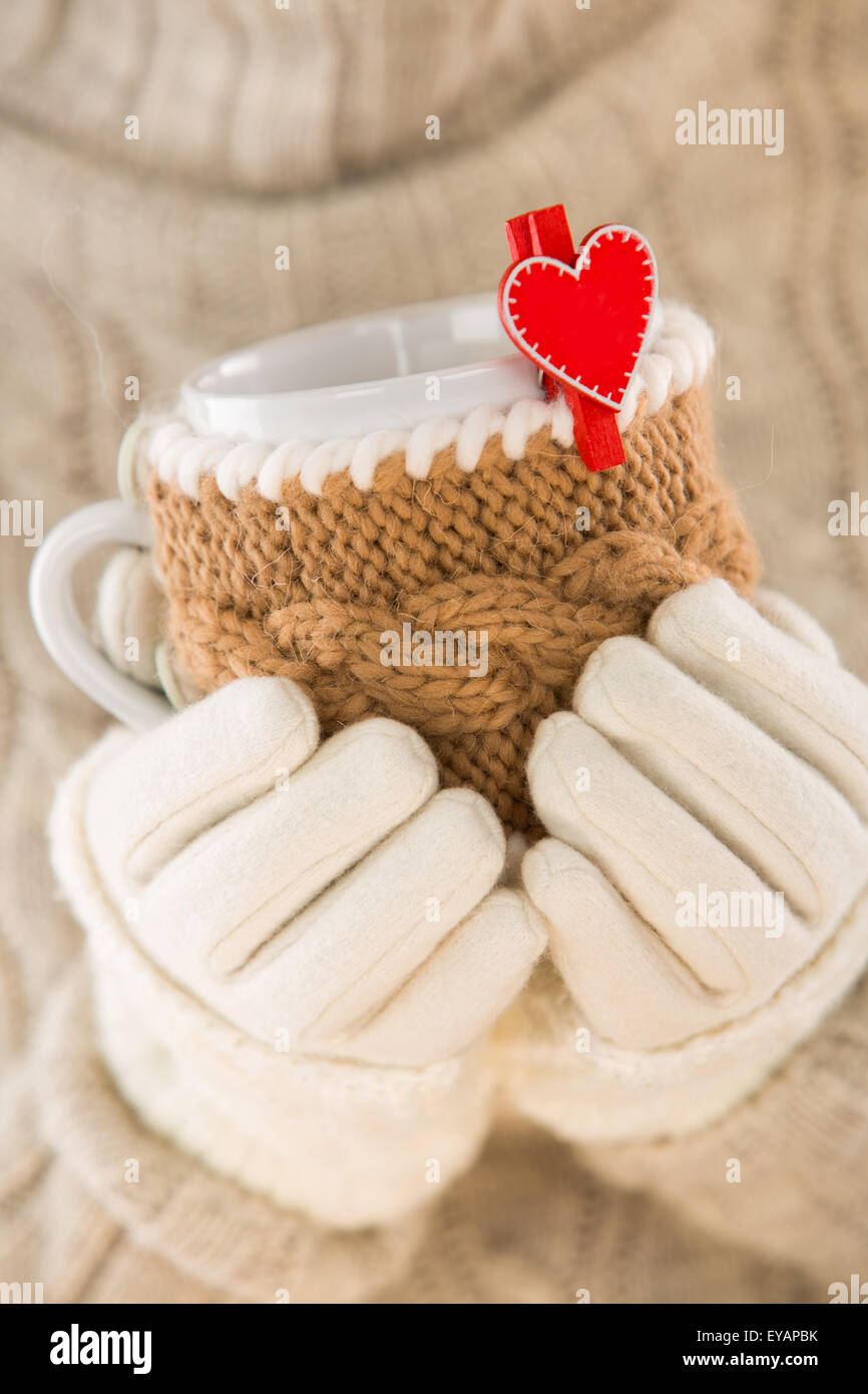 Knitted wool cup in human hands. With red hearts and the word love. Stock Photo