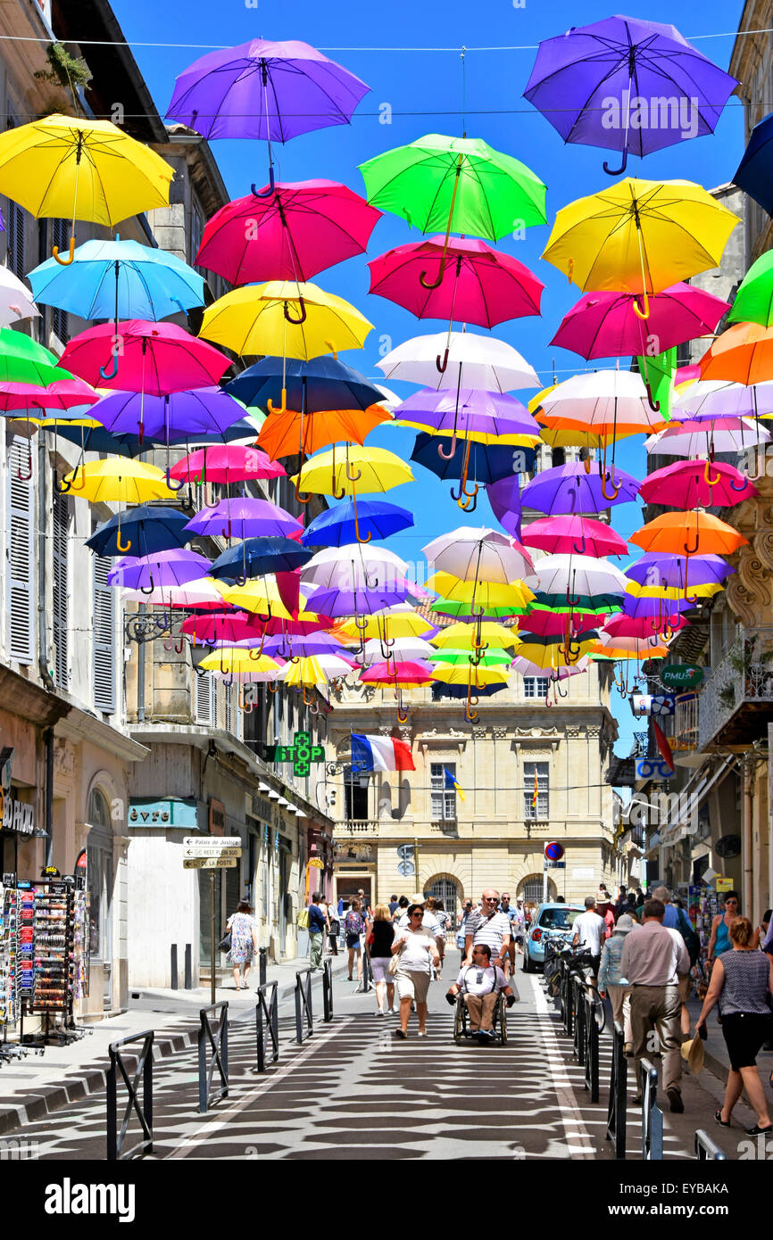 Sunshine blue sky & umbrella colours street art display ancient City of Arles France Provence cast repetitive shadow patterns across shopping street Stock Photo