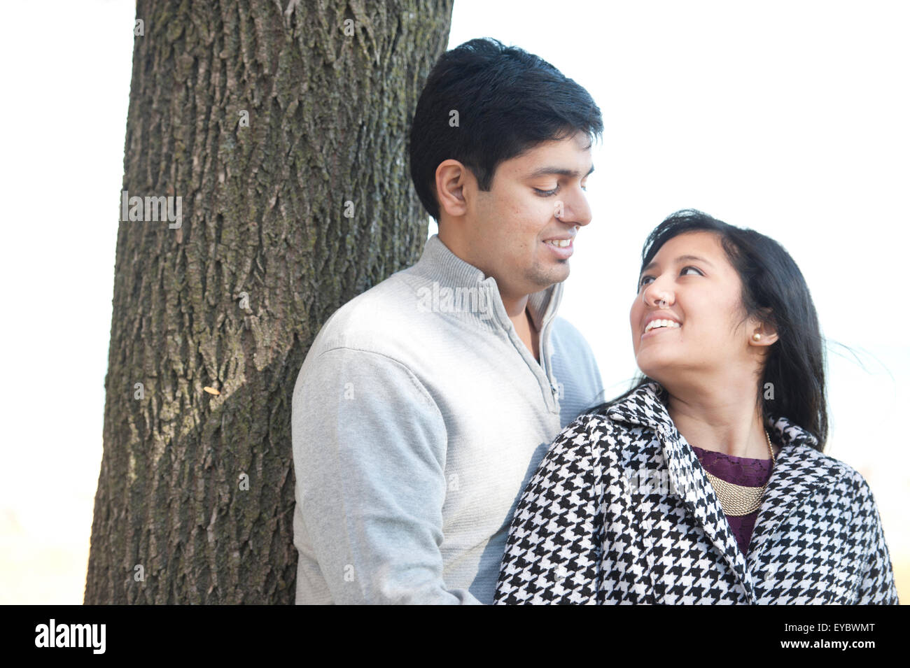 A young and happy Indian couple posing by a tree in the Fall on a sunny ...