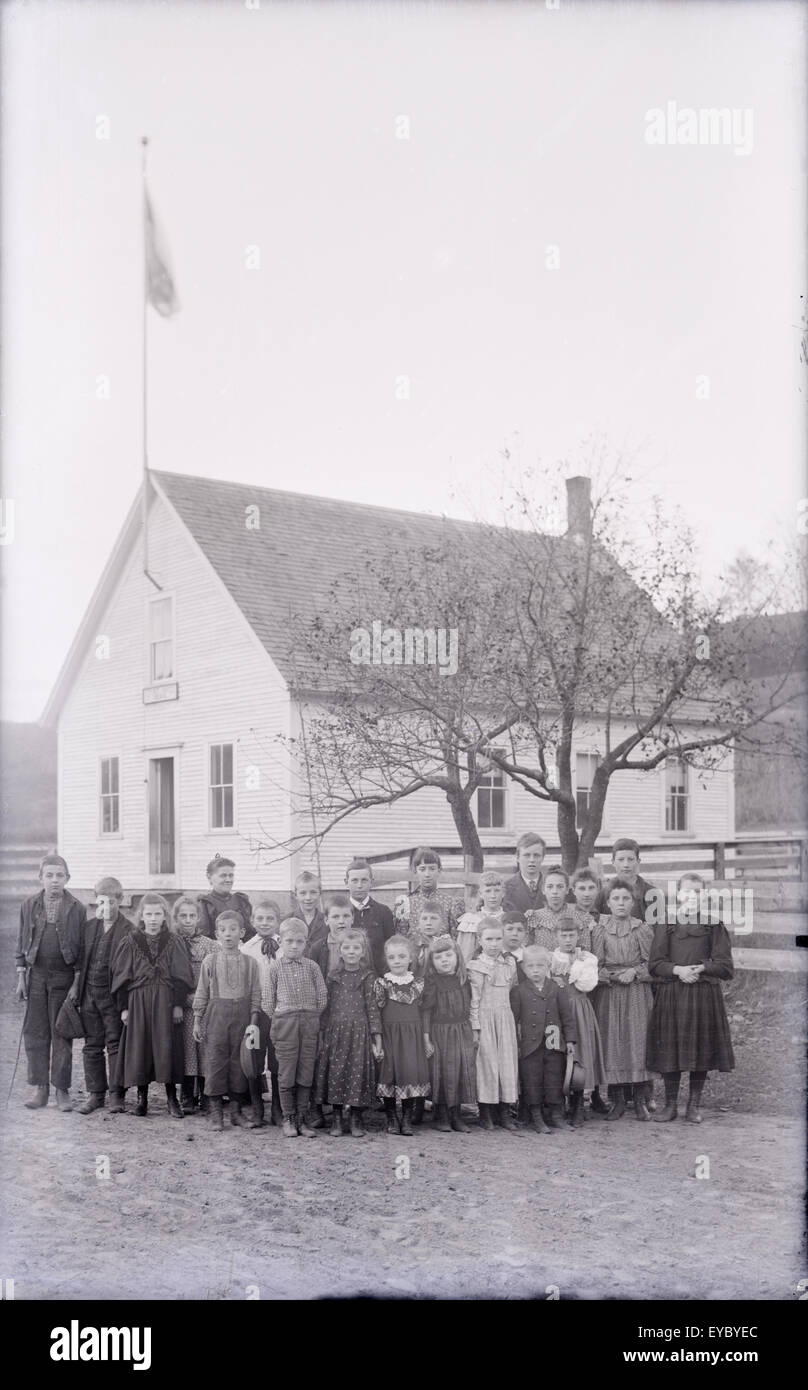 Antique c1900 photograph of a one-room schoolhouse and students with teacher. There is an 1888 date on the school building's plaque. Location is USA; more specific information is not available. Stock Photo