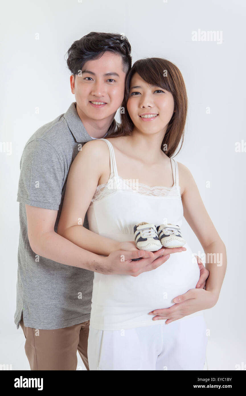 Young man embracing pregnant woman and holding a pair of shoes together ...