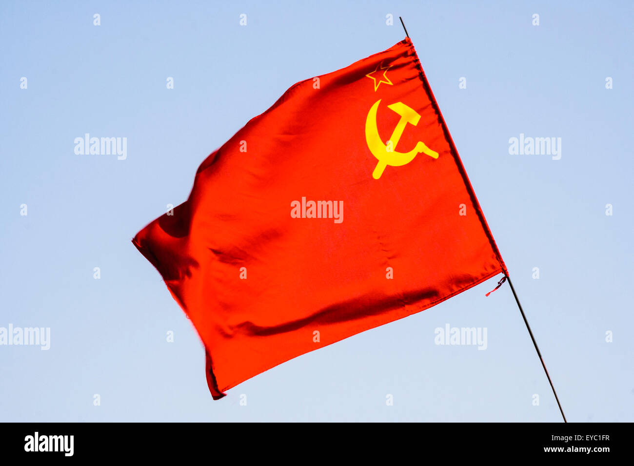 Communist flag of Russia, red flag, with yellow star outline and hammer and sickle below that. Blue sky background. Stock Photo