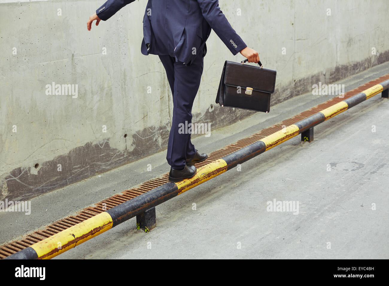 Rear view of businessman with briefcase balancing on yellow-and-black road curb Stock Photo