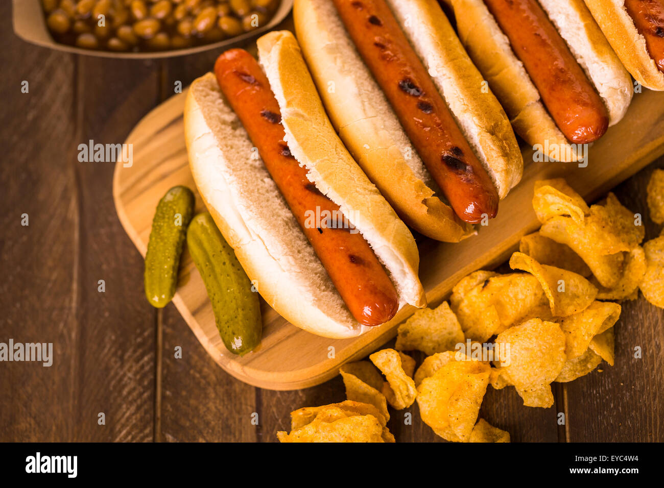 Grilled hot dogs on a white hot dog buns with chips and baked beans on