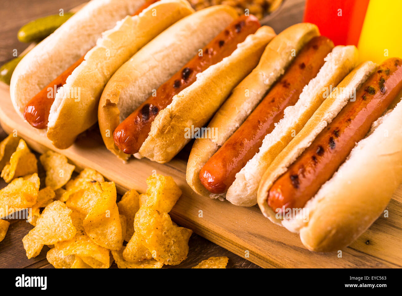 Grilled hot dogs on a white hot dog buns with chips and baked beans on