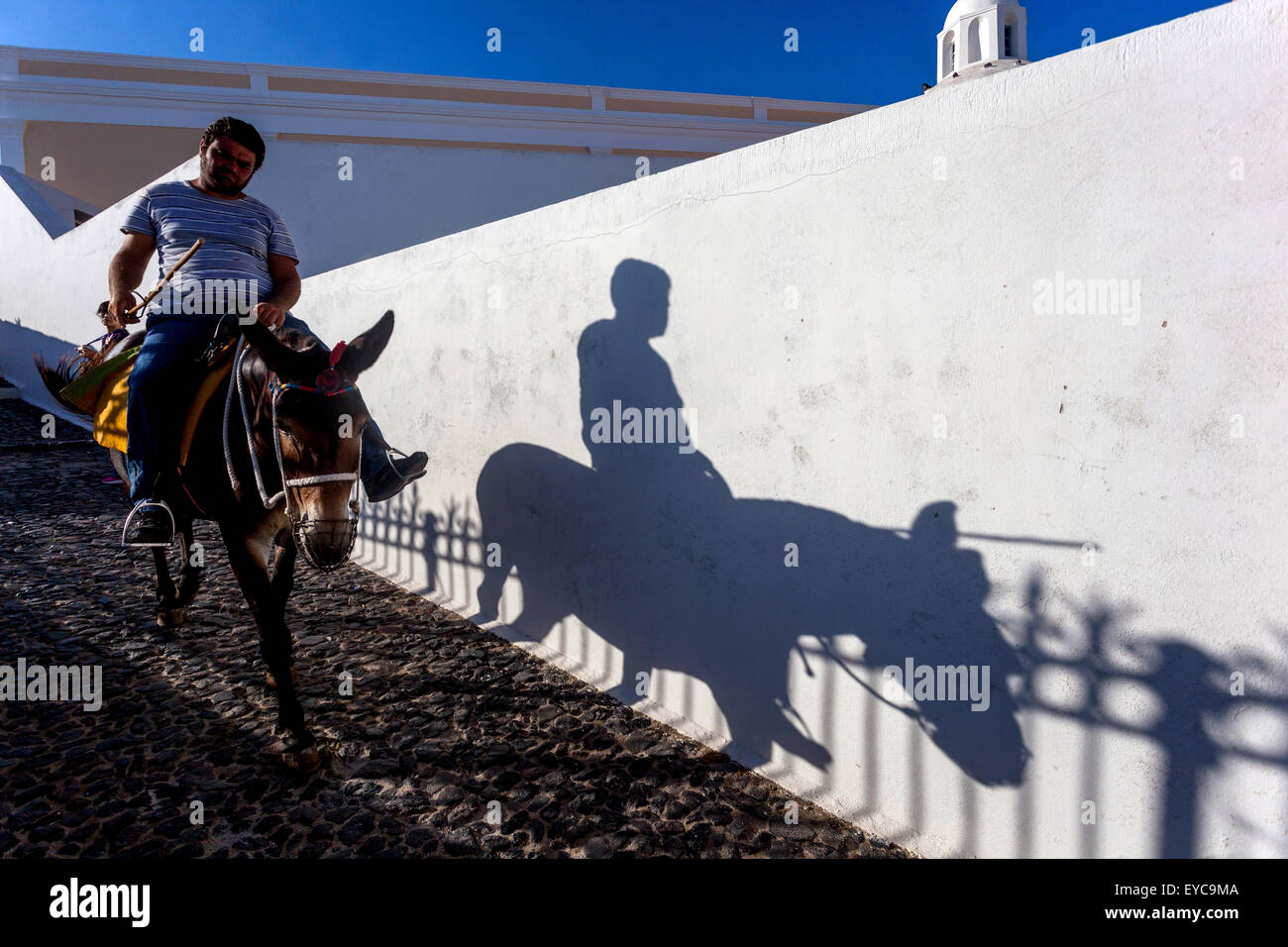 A man on a donkey, Fira Santorini street Cyclades Greek Island, Greece shadow wall Stock Photo