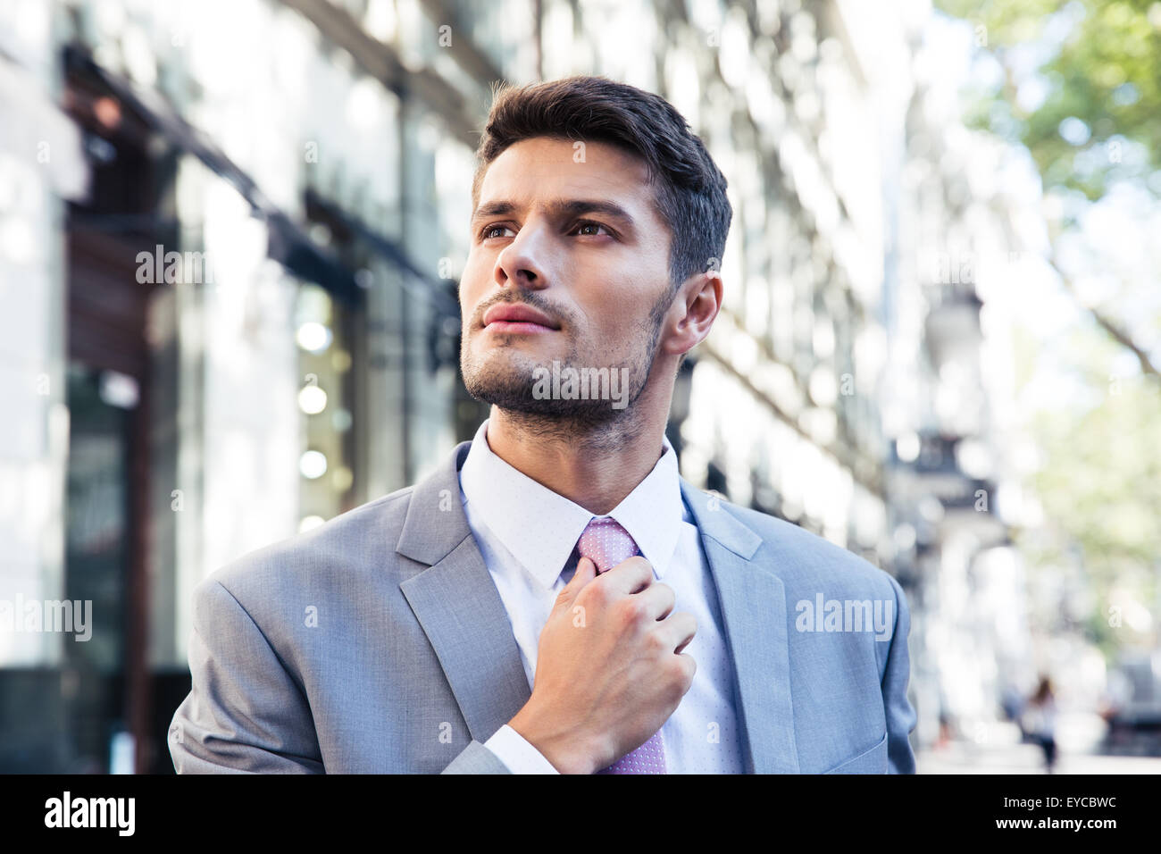 Confident businessman straightens his tie outdoors Stock Photo