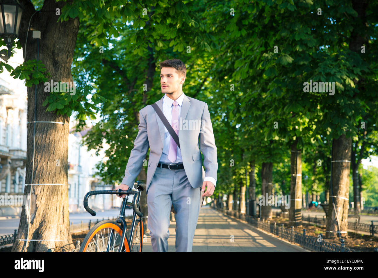 Handsome businessman walking with bicycle in park Stock Photo