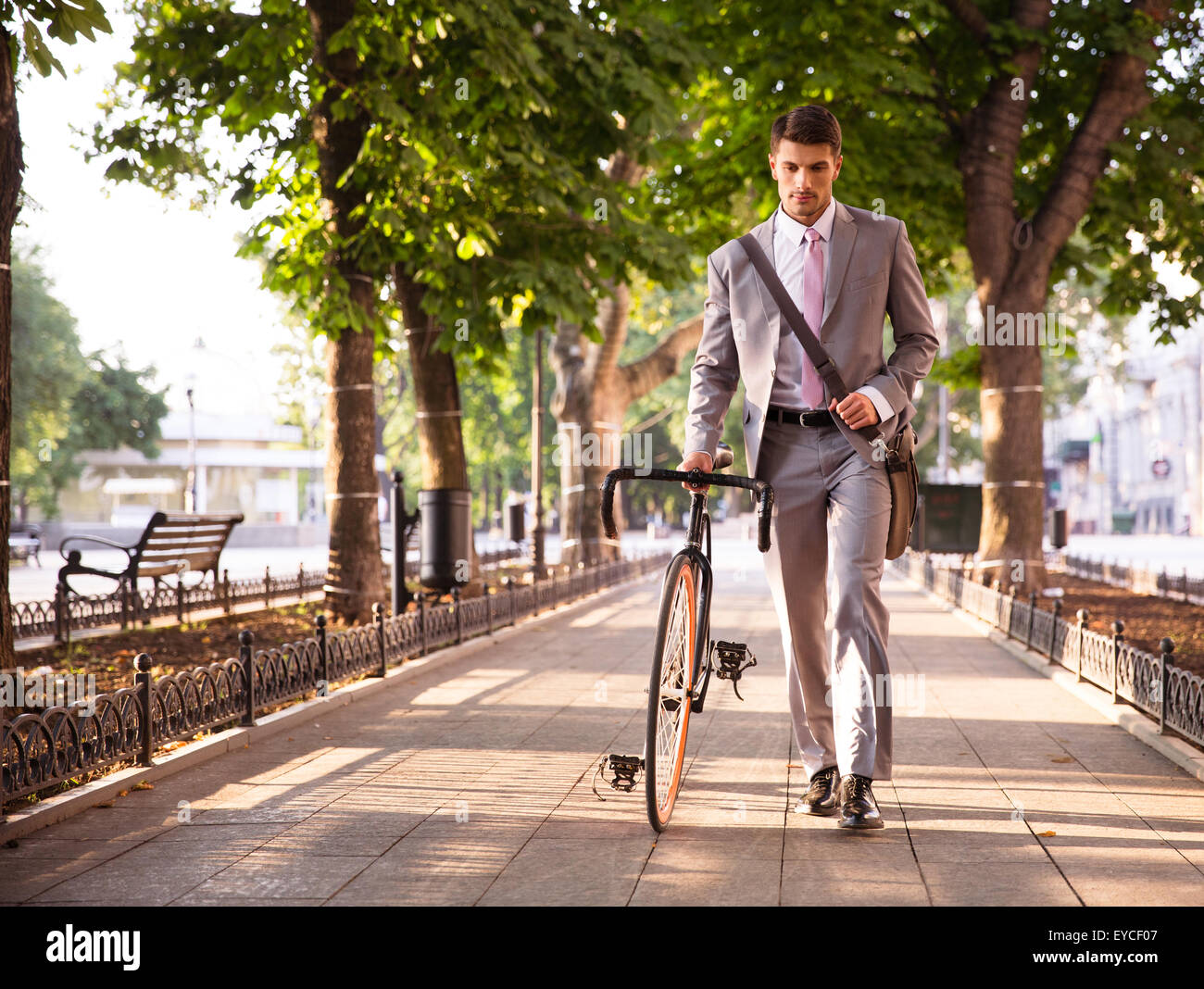 Pensive young businessman walking with bicycle on the street in town Stock Photo