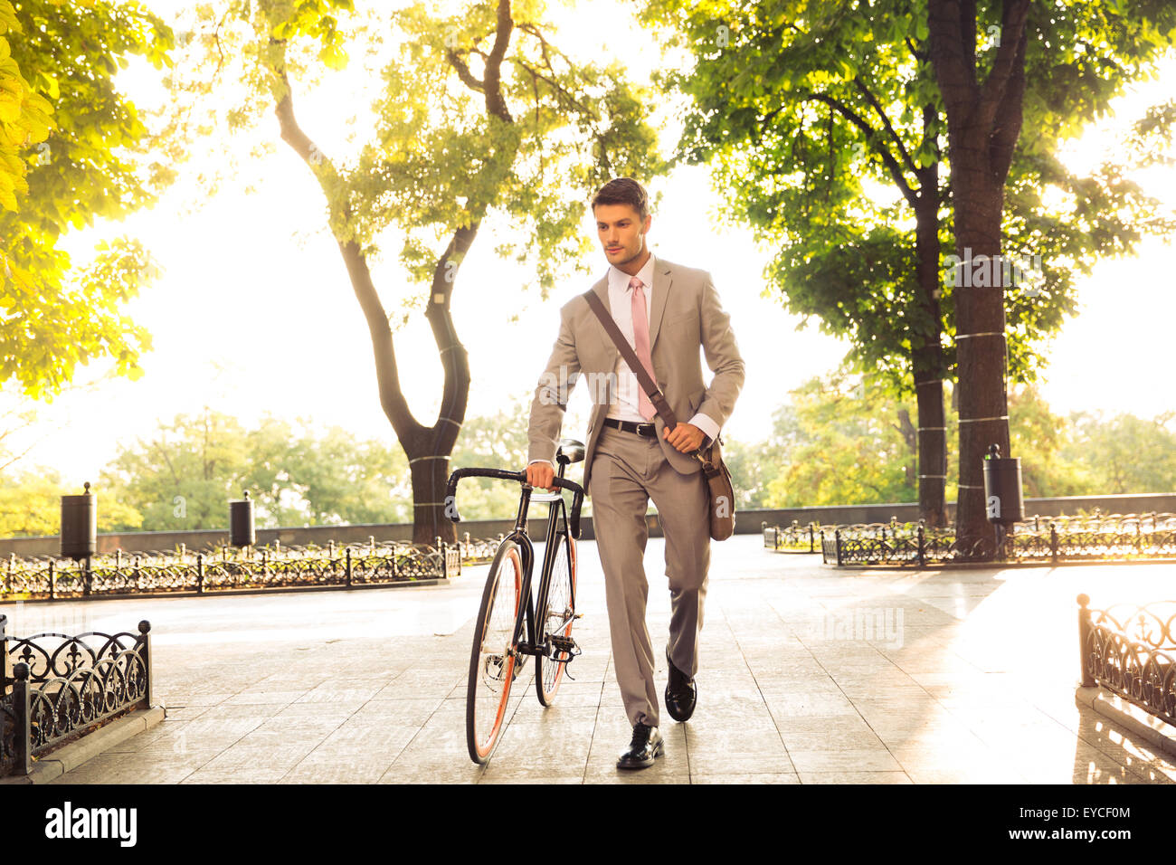 Confident young businessman walking with bicycle on the street in town Stock Photo