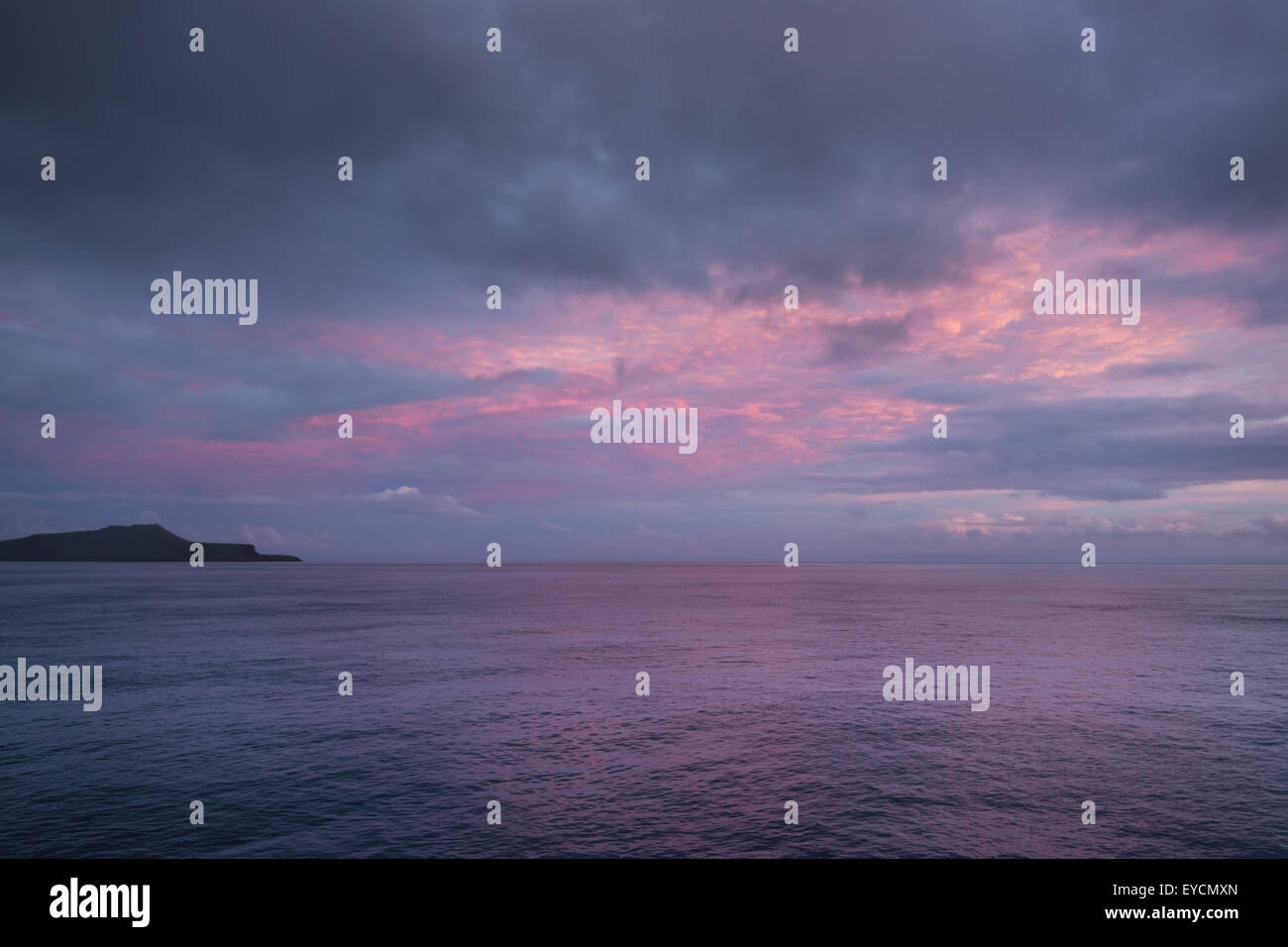 Blue hour with orange clouds near Floreana. It is still so dark, no detail is visible on land Stock Photo
