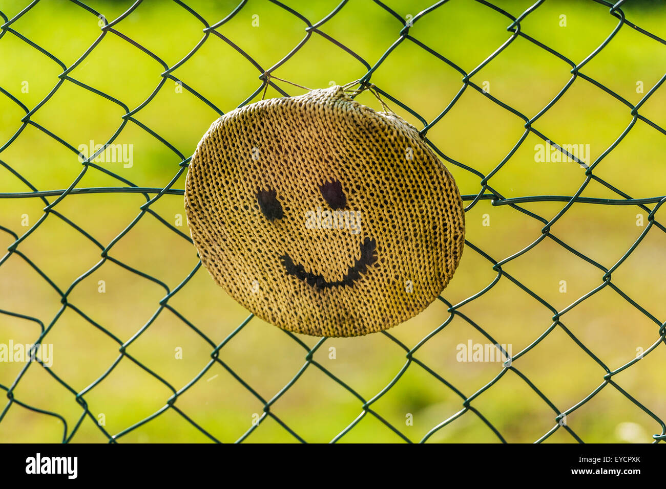 Knitted smiley face fixed on wired fence Stock Photo