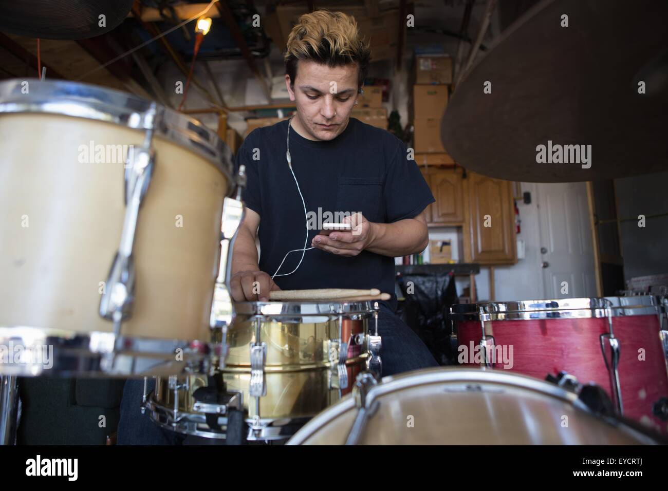 Young male drummer in basement reading smartphone texts Stock Photo