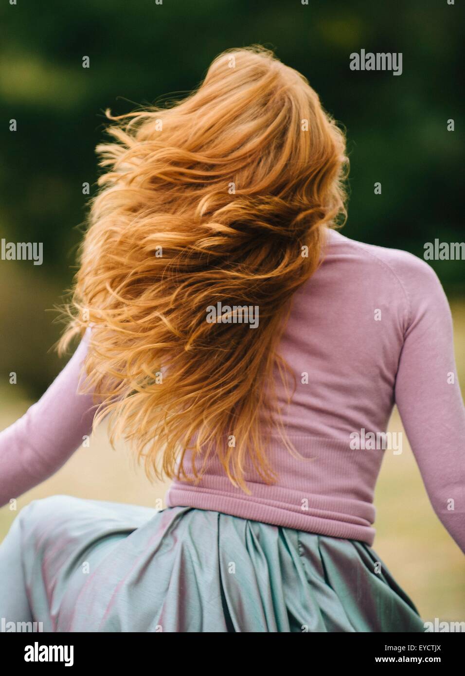 Rear view of young woman with long red hair twirling in park Stock ...