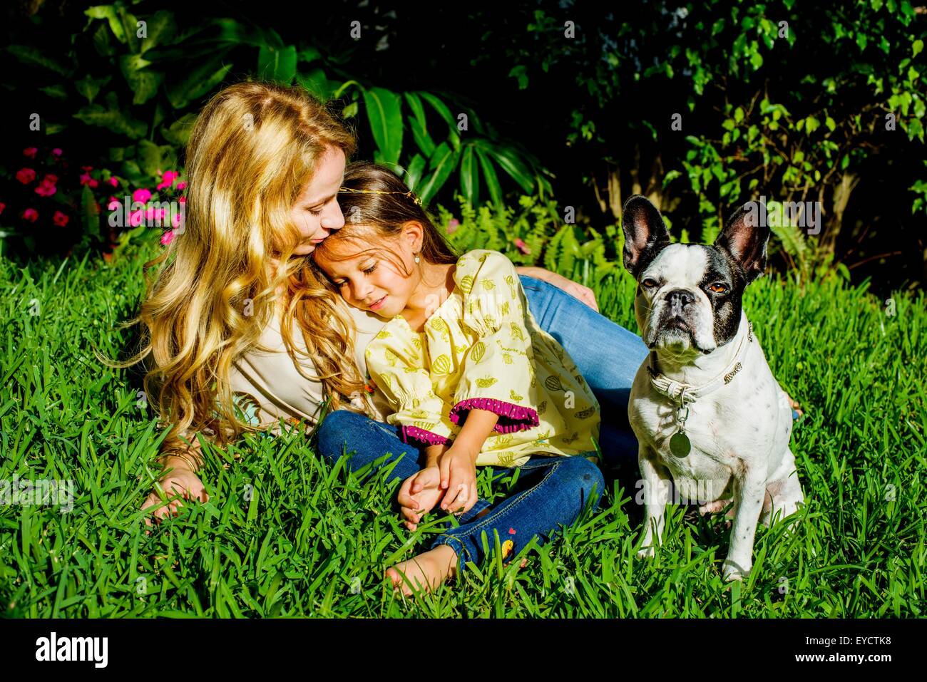 Mature woman, daughter and dog sitting in garden grass Stock Photo
