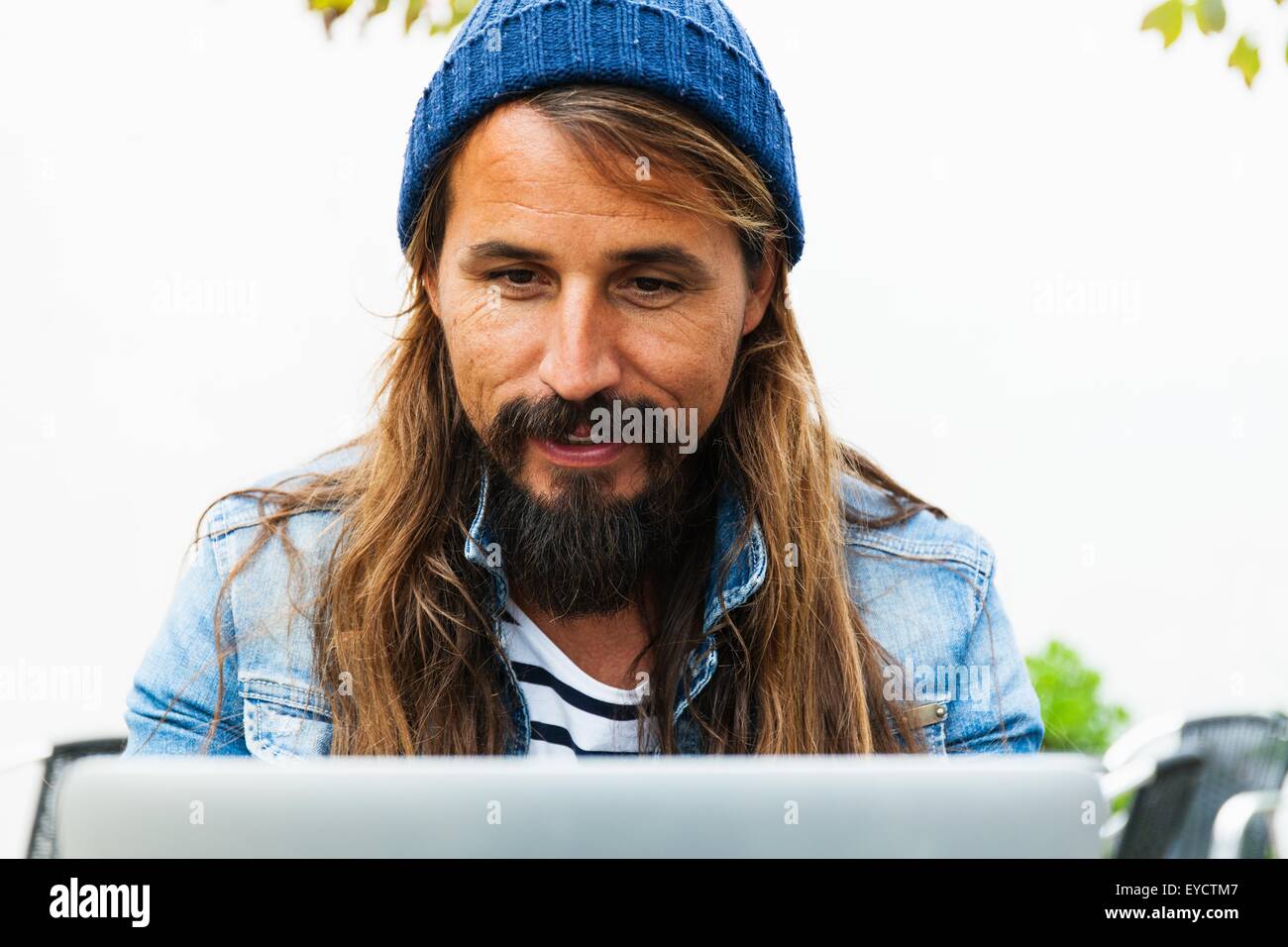 Mid adult man wearing hat using laptop Stock Photo