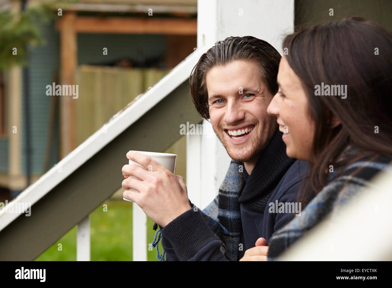 Young couple sitting on porch step drinking coffee Stock Photo