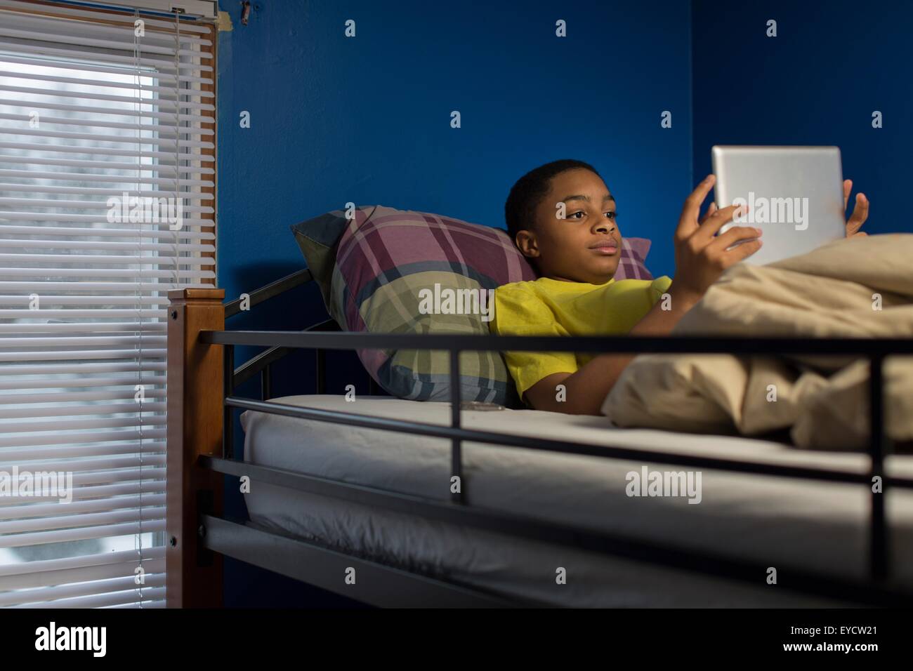 Teenage boy lying in bunkbed browsing digital tablet Stock Photo