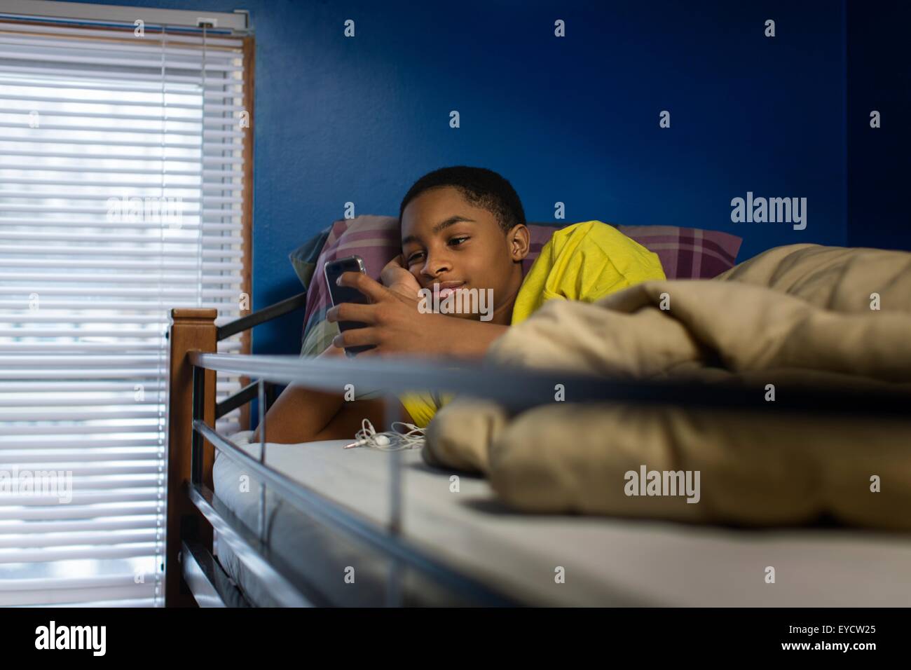 Teenage boy lying in bunkbed reading smartphone text Stock Photo
