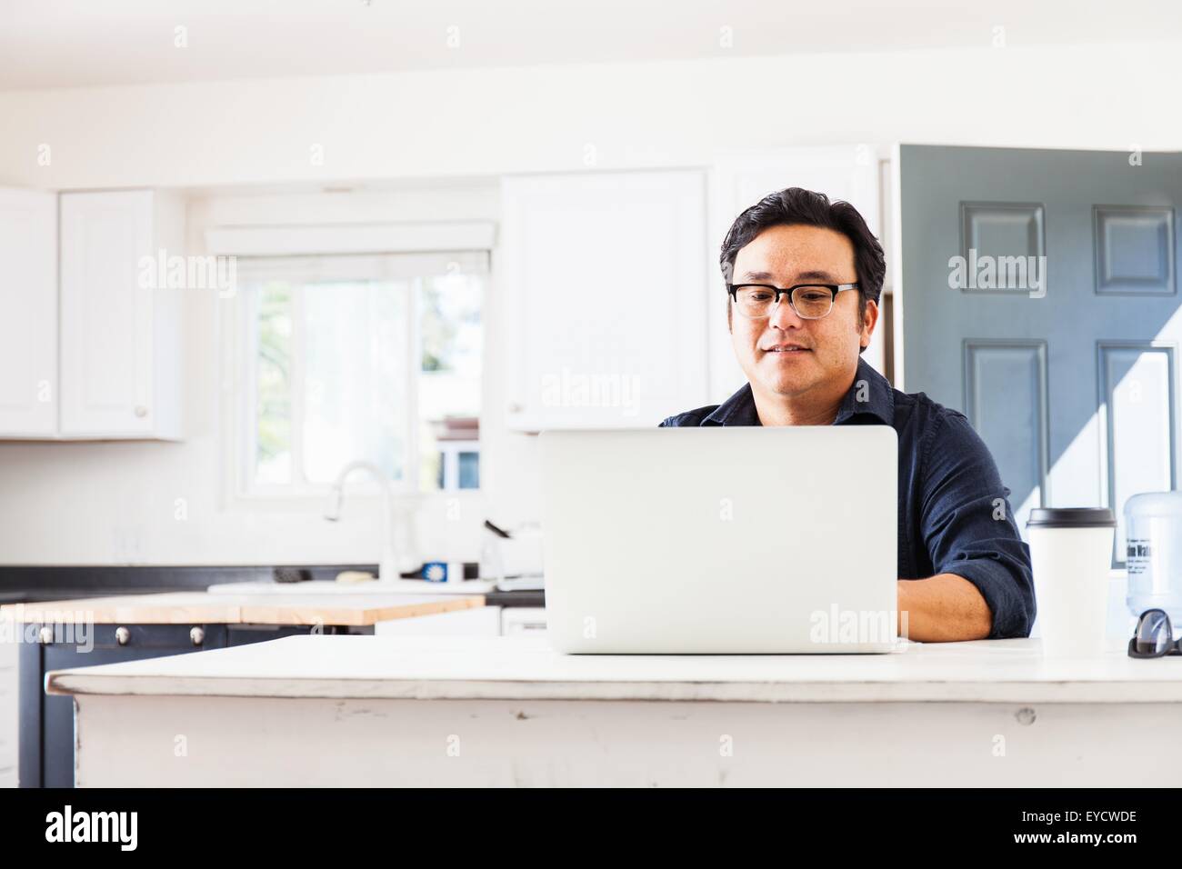Mature businessman typing on laptop in kitchen Stock Photo