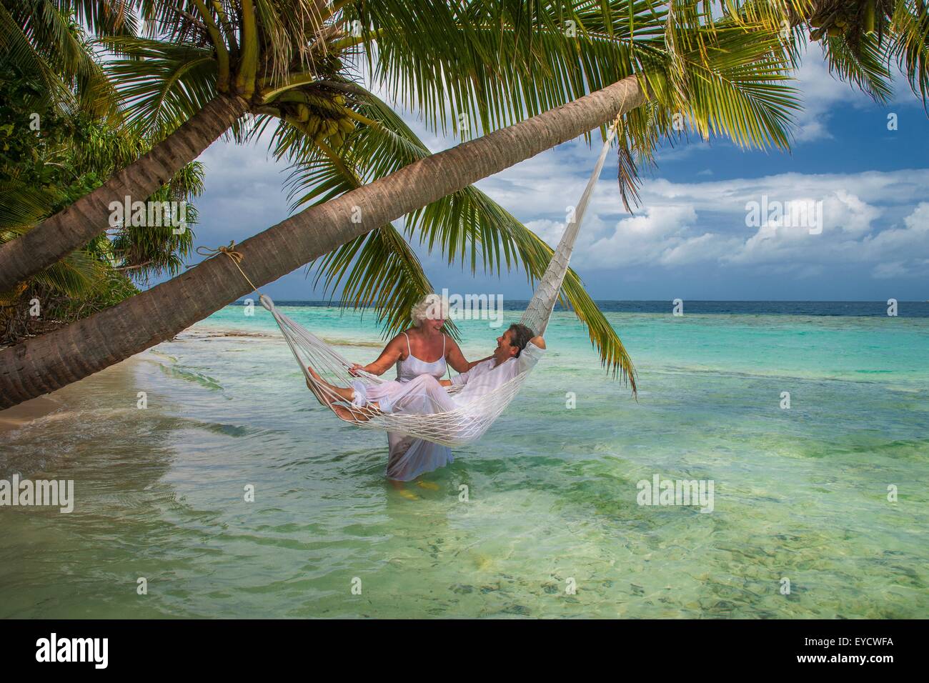 Senior man relaxing in hammock with woman, Maldives Stock Photo