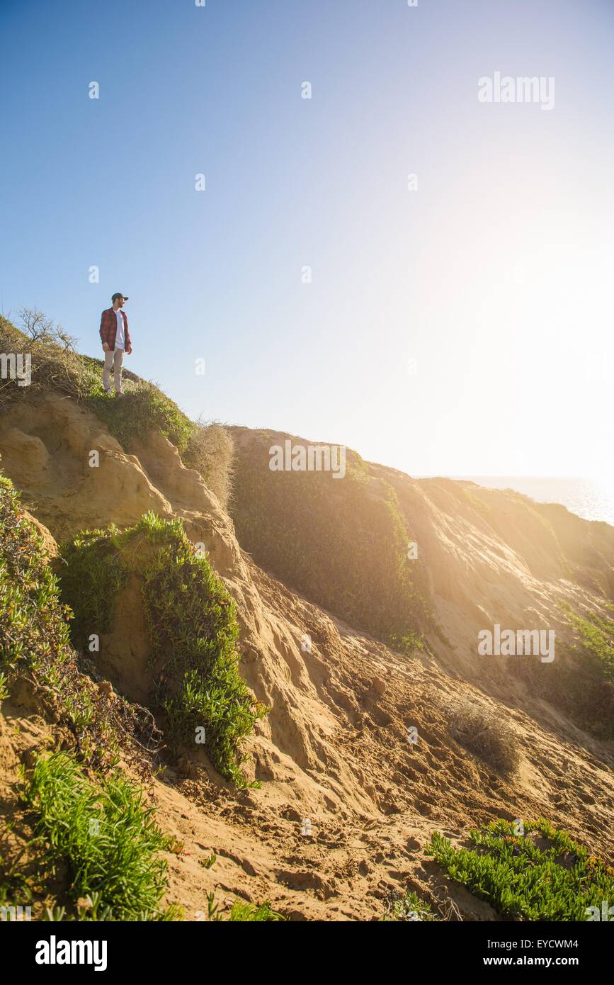 Young man standing at top of sandy hill, looking at view Stock Photo