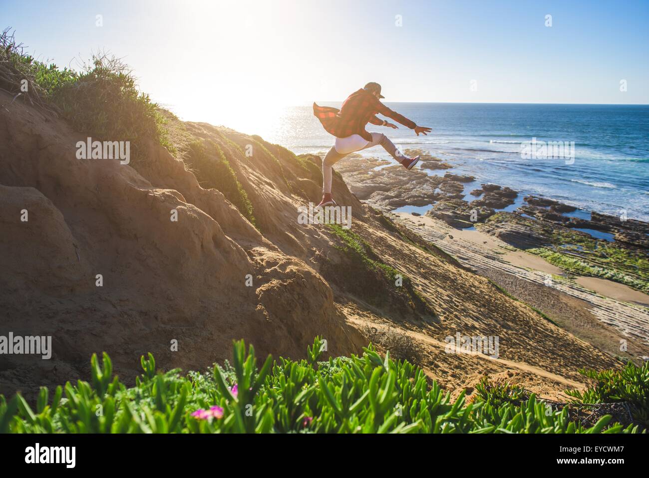 Young man jumping down sandy hill, in mid air Stock Photo