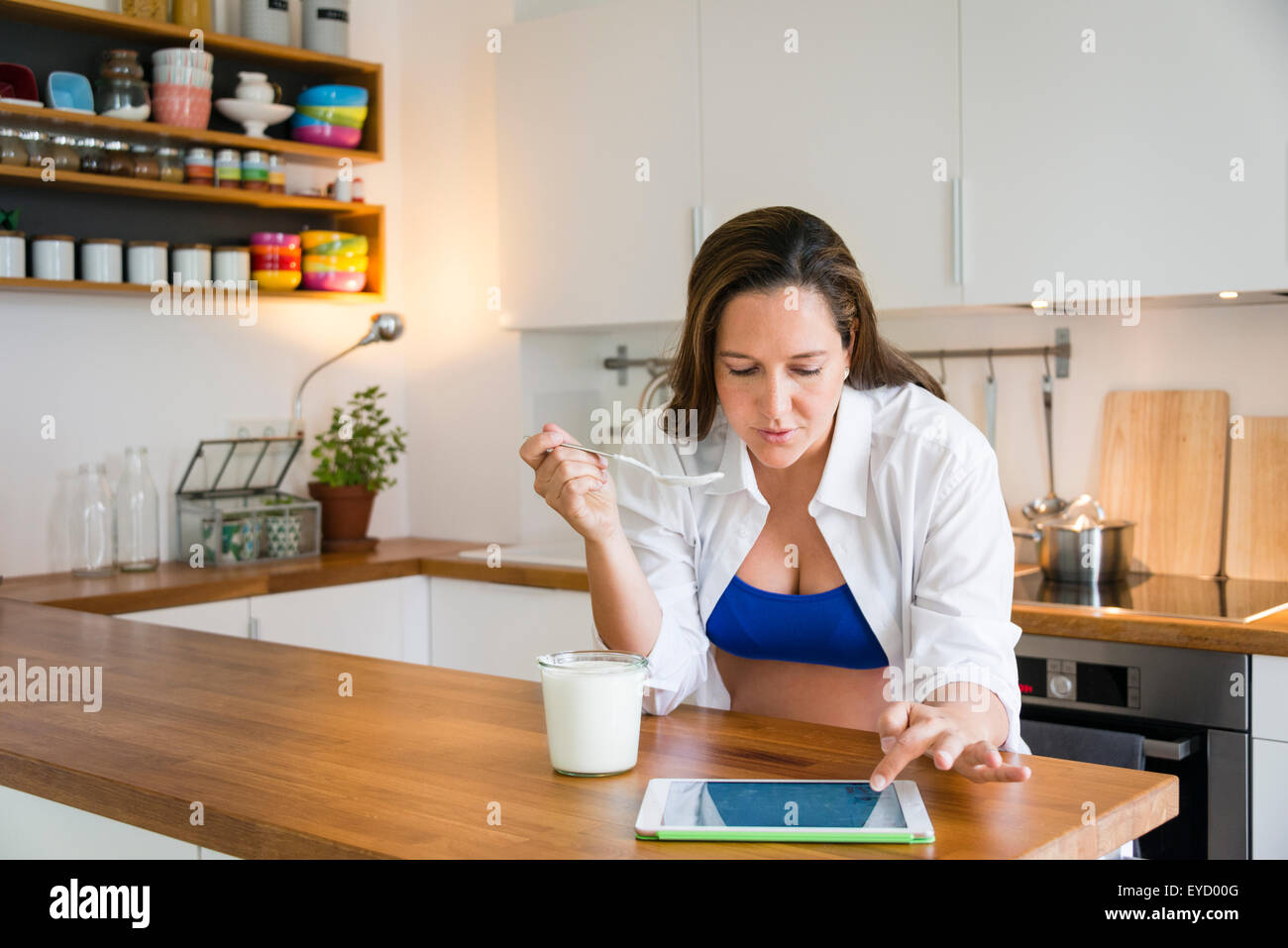 Pregnant woman eats yogurt while using tablet Stock Photo Alamy