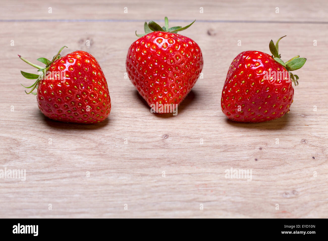 three fresh strawberries on a wood table Stock Photo - Alamy