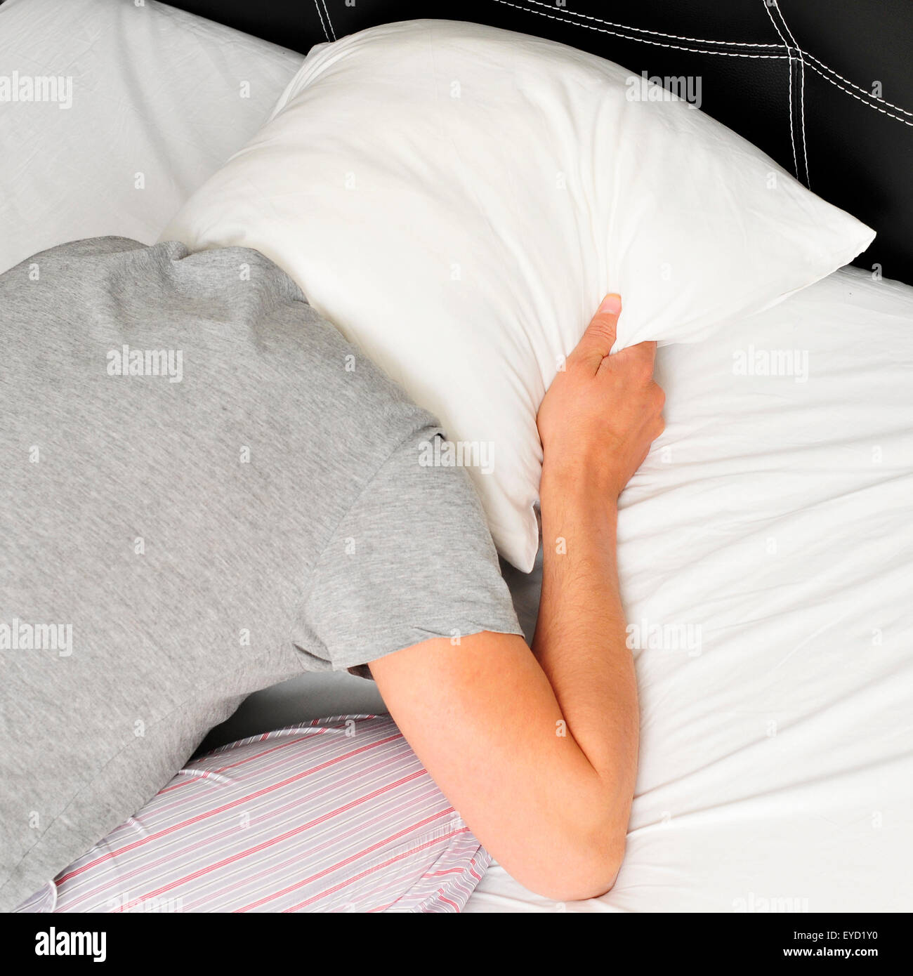 closeup of a young man face down in bed covering tightly his head with