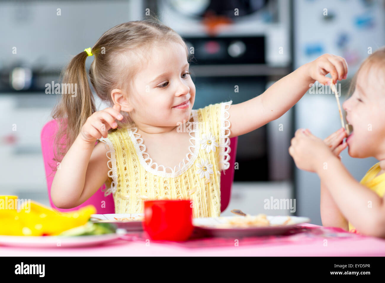 kids eating spaghetti with vegetables in nursery Stock Photo