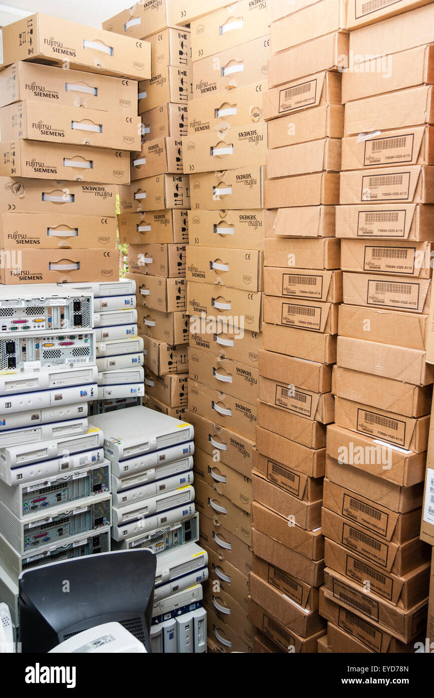 Junked computers stored in room. Stacked cardboard computer base boxes with piles of white computer bases in front awaiting collecting after upgrade. Stock Photo