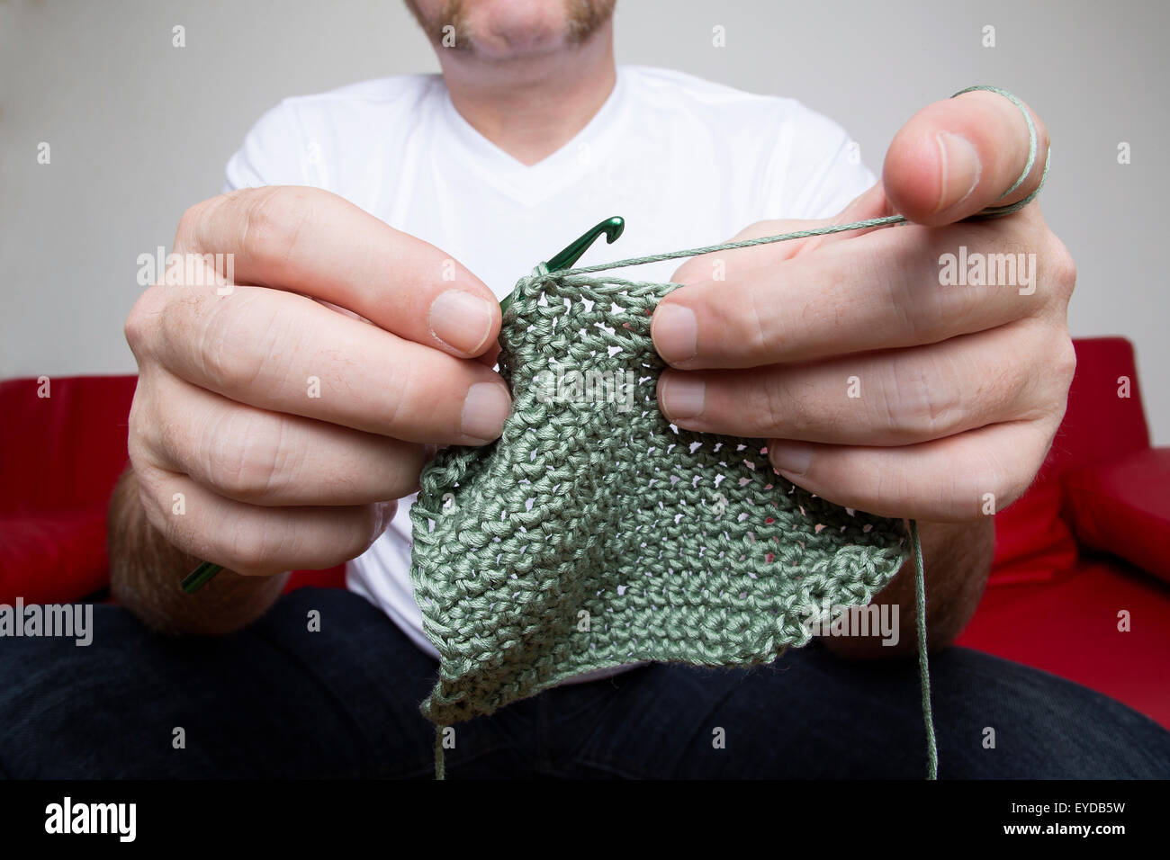 Closeup of a man knitting a scarf on a red sofa Stock Photo