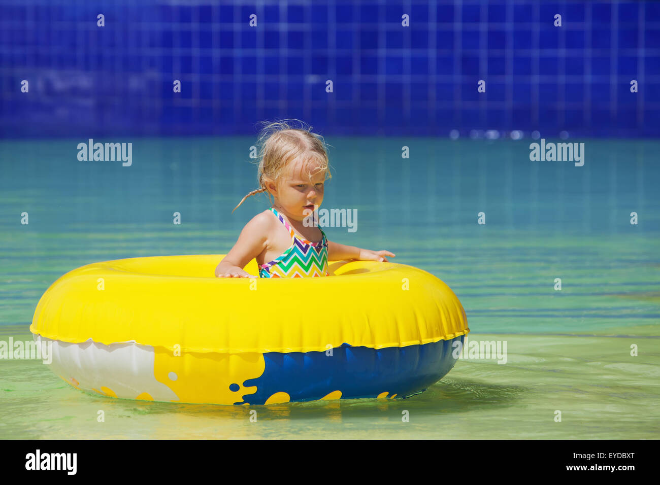 Funny portrait of cheerful baby girl swimming with fun on yellow tube