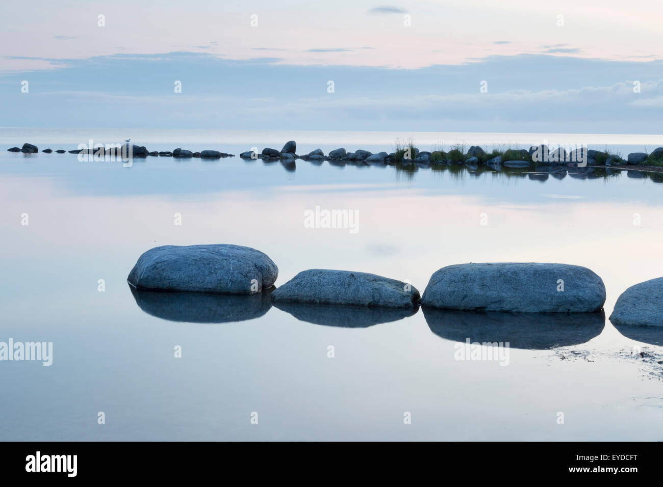 Breakwater Rocks in Calm Sea with clouds and reflections in the water. Stock Photo