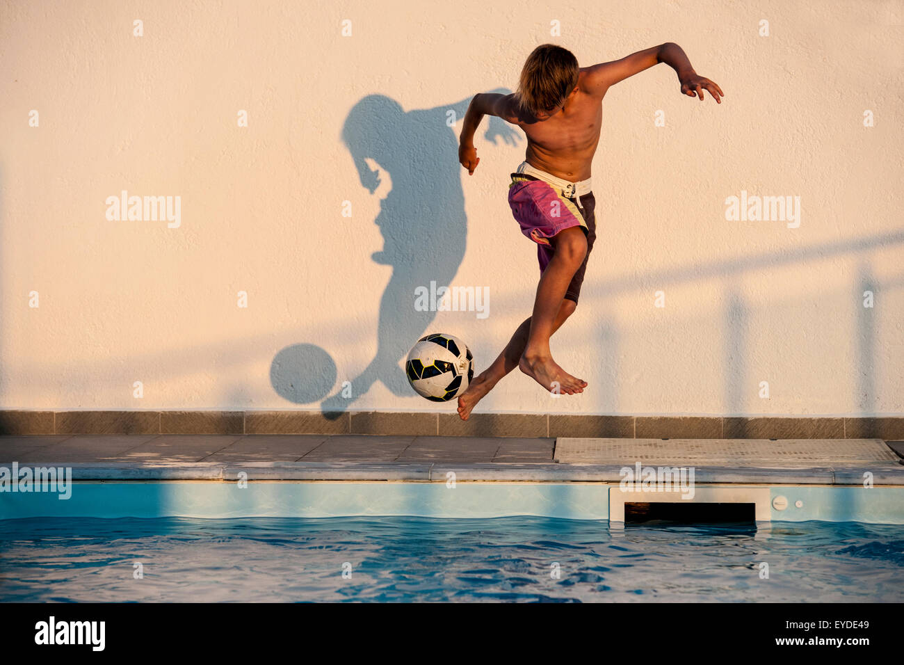 A boy playing football on holiday by a swimming pool. Stock Photo