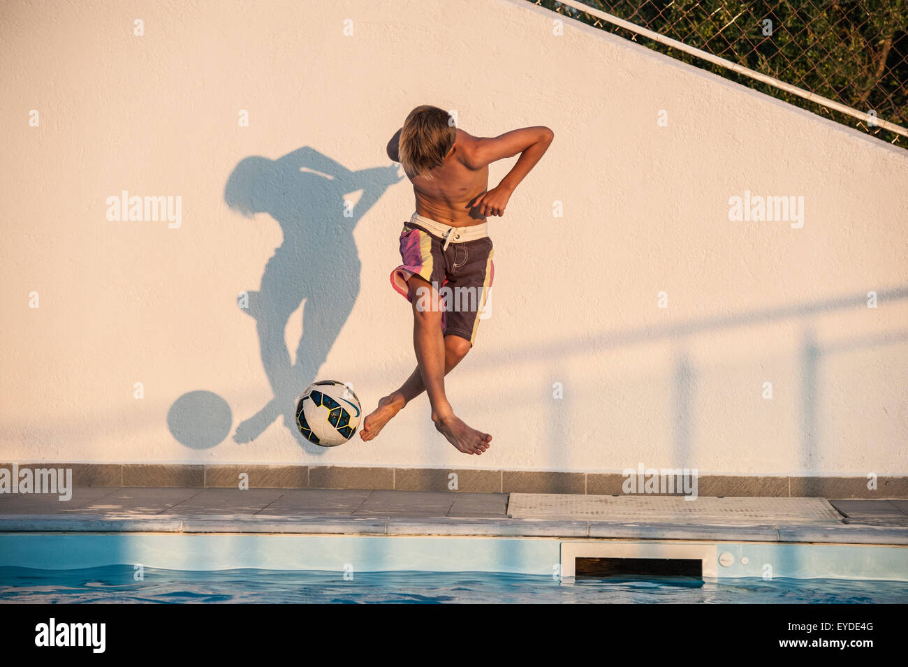 A boy playing football on holiday by a swimming pool. Stock Photo