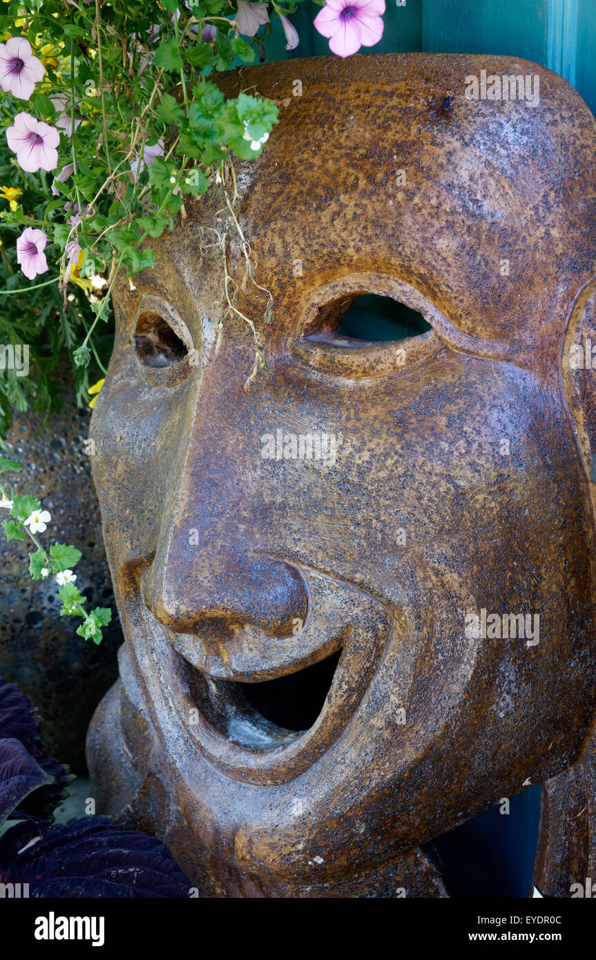 Large ceramic laughing face in a flower garden Stock Photo