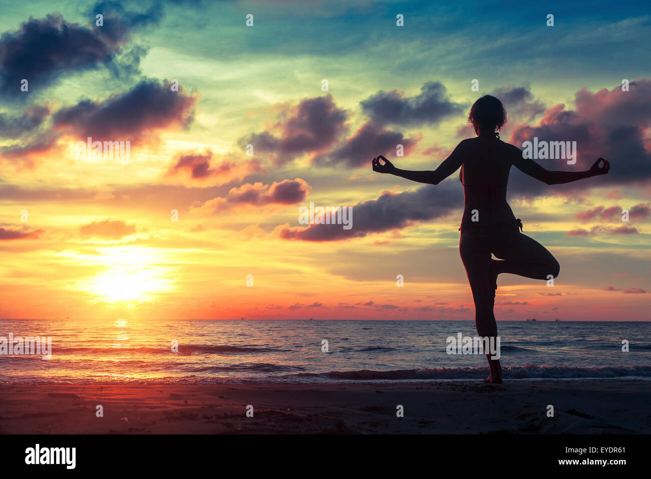 Silhouette of woman standing at yoga pose on the ocean beach during an ...