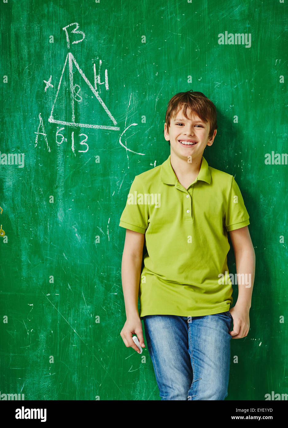 Happy schoolboy standing by blackboard with geometric task on it Stock Photo