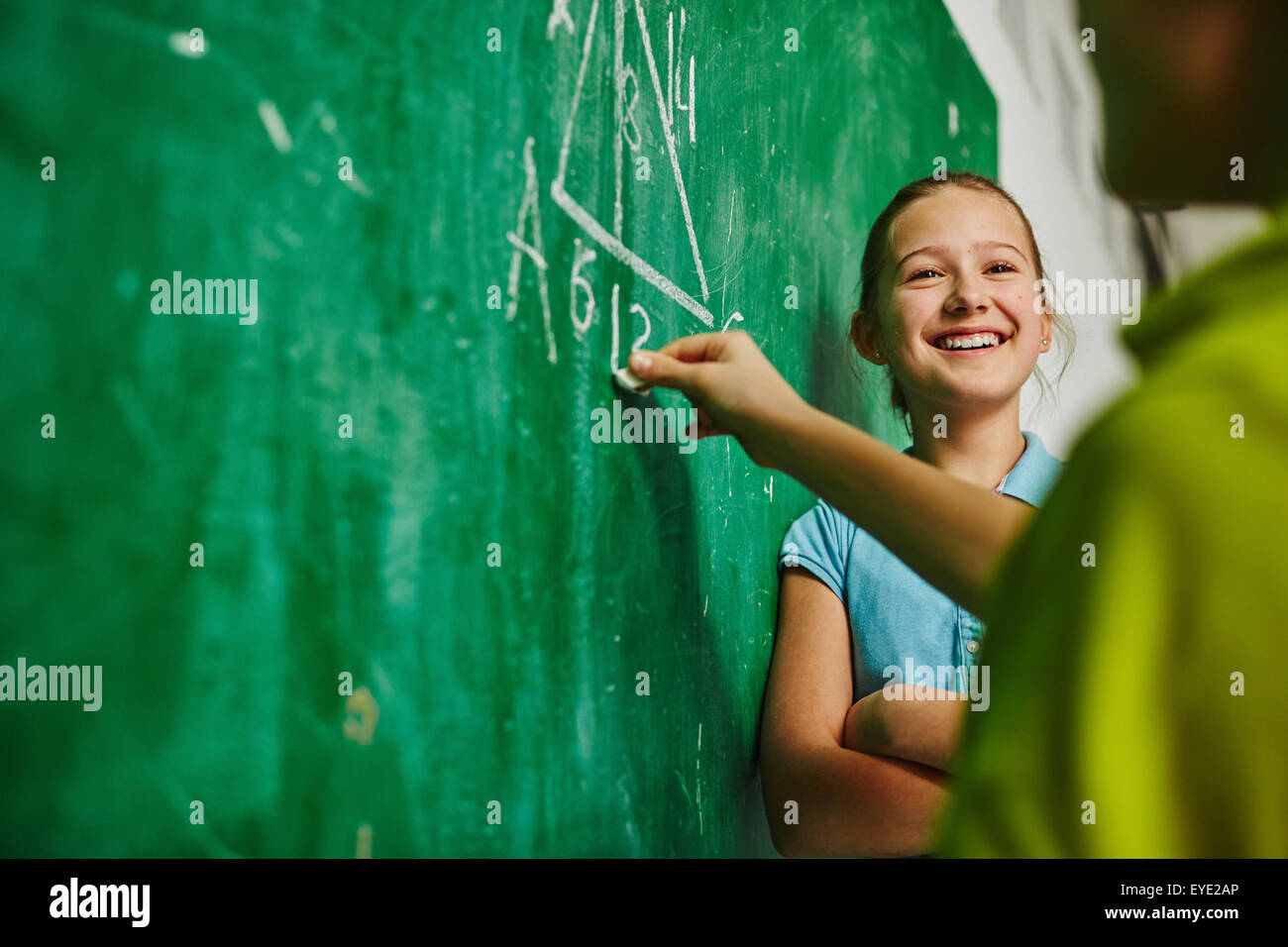 Successful schoolgirl looking at classmate while he explaining geometric task on blackboard Stock Photo