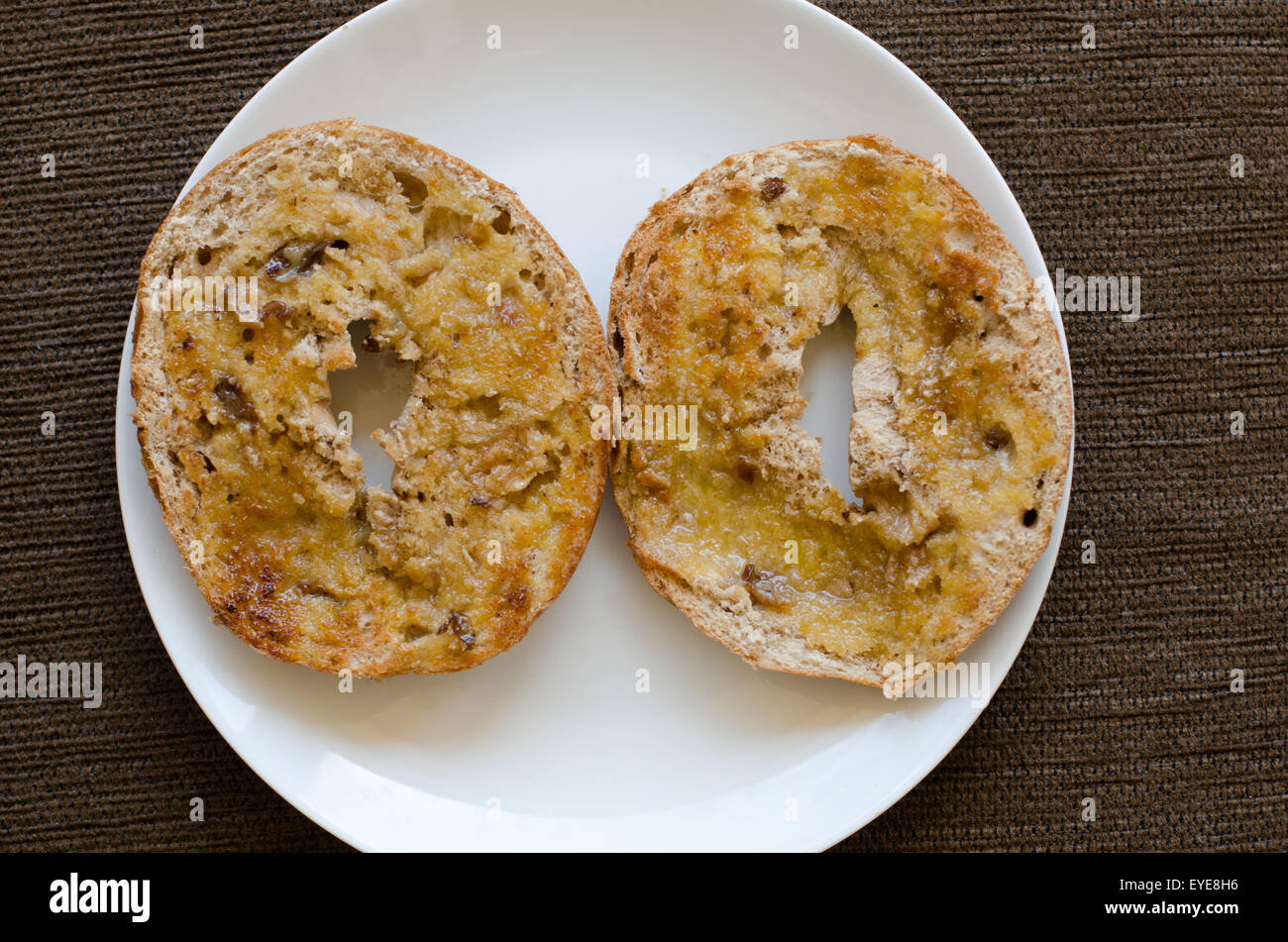 Two halves of a toasted raisin bagel with butter on a white plate Stock Photo