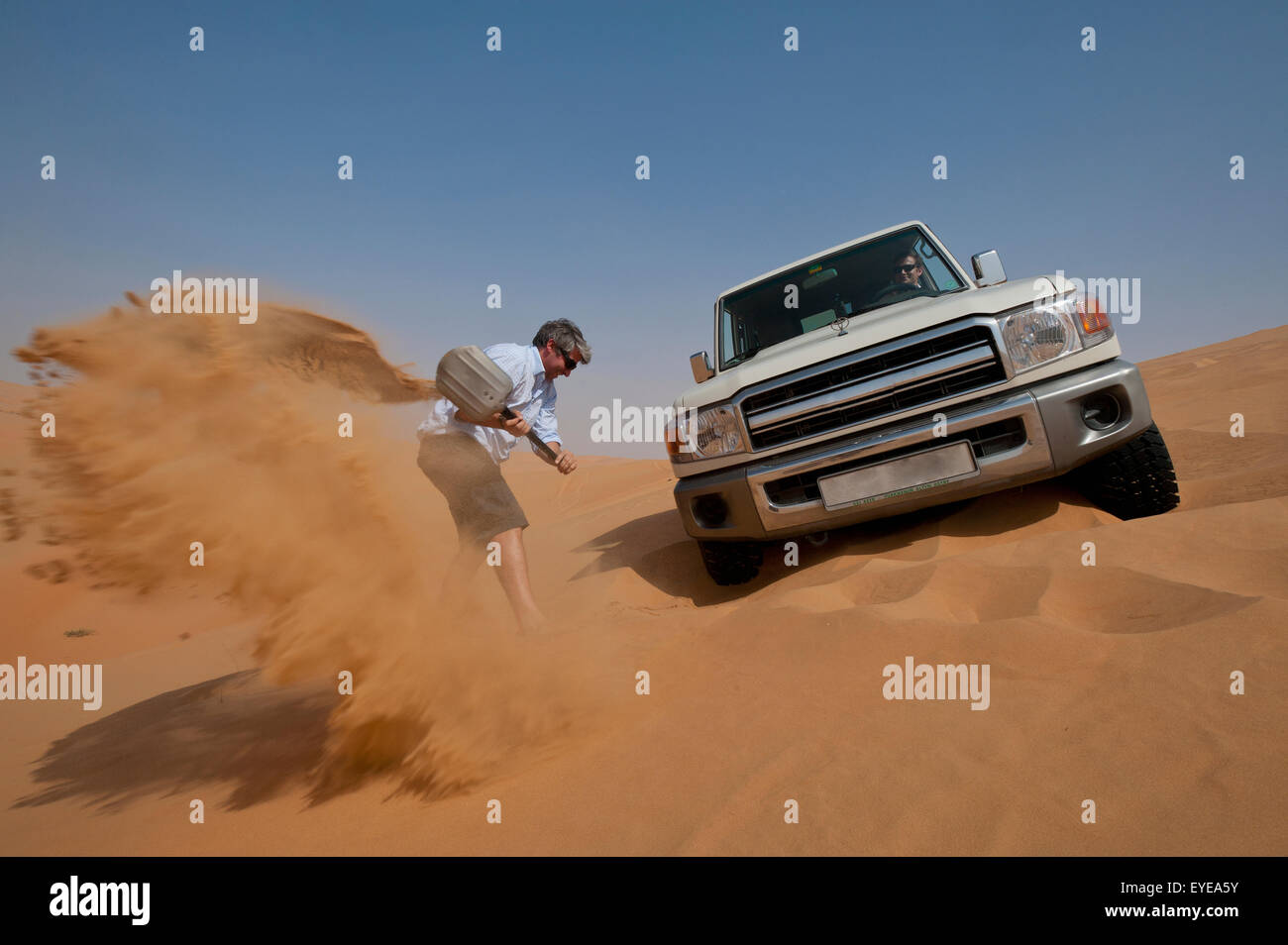 UAE, Abu Dhabi, Man trying to dig out 4 wheel drive stuck in soft sand