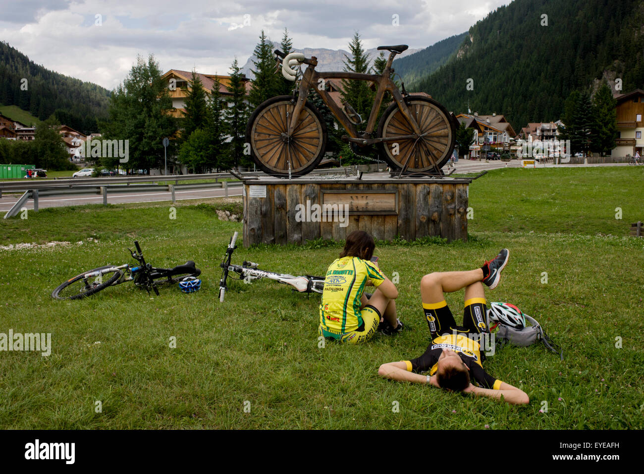 Cyclists rest by a large wooden mountain bike sculpture in the town of Corvara during the summer walking season in south Tyrol. Stock Photo