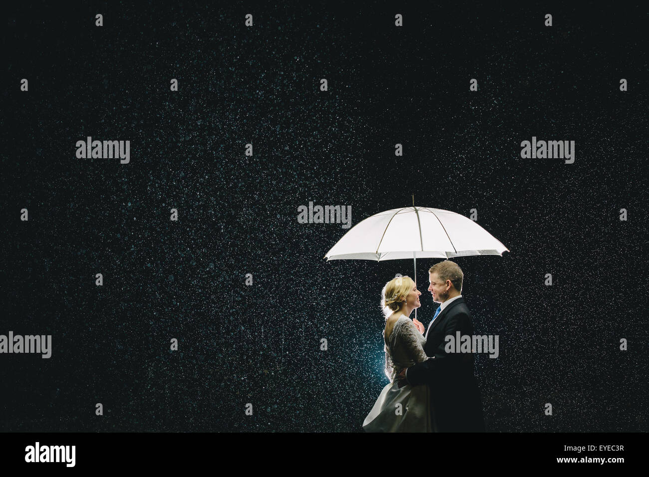 Portrait of Bride & Groom beneath an umbrella in the rain backlit with flash Stock Photo