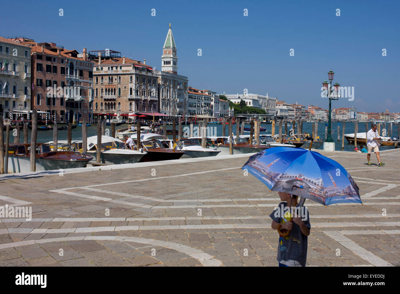 A boy carries a Venice picture umbrella in front of Santa Maria della Salute church in Dorsoduro, overlooking the Grand Canal Stock Photo