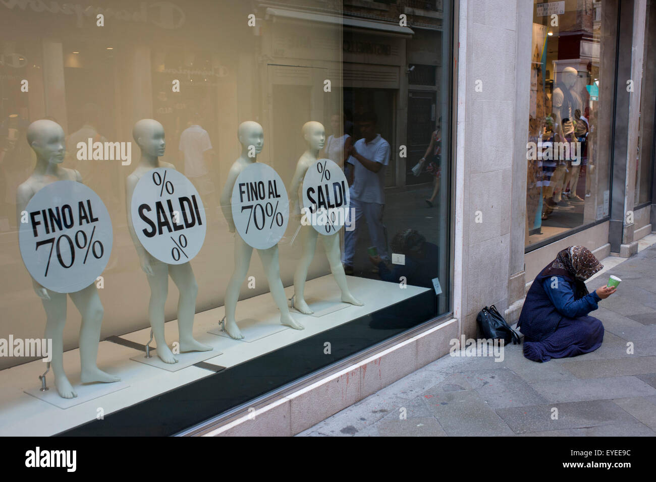 Retail mannequins advertising a 70% sale with a woman street beggar in the San Marco shopping district of Venice, Italy. Stock Photo